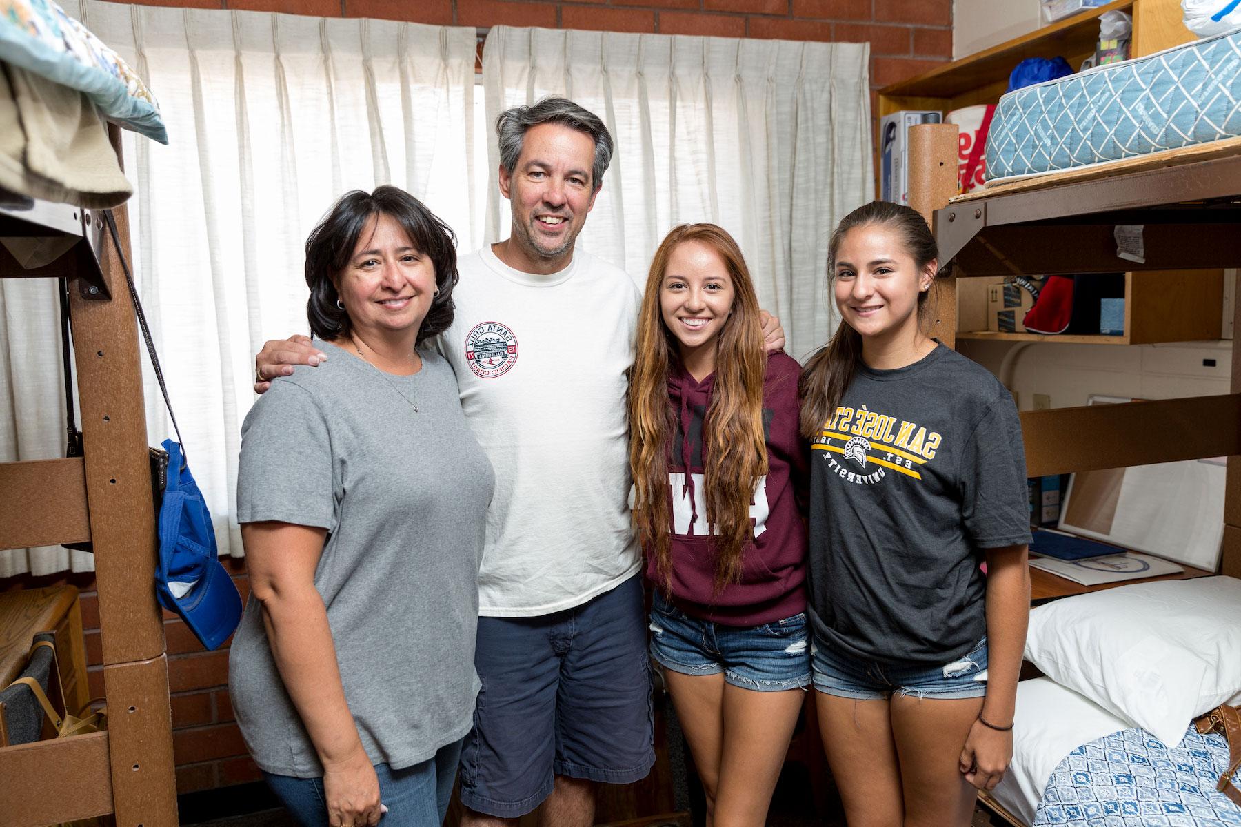 Freshman students posing with their parents in the dorm.